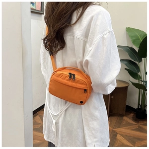 Detail of bright orange nylon crossbody bag featuring dual zippers and adjustable strap