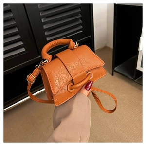 Detailed macro view of orange-brown litchi pattern leather texture on a compact handbag