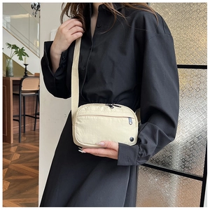 Close-up of minimalist off-white nylon crossbody bag with dual black zipper compartments