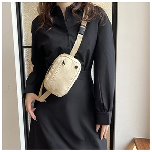 Detail of beige nylon crossbody bag featuring adjustable straps and plastic buckle closure