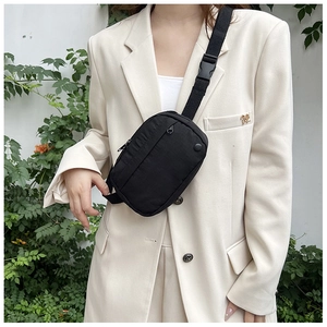 Close-up of black minimalist nylon crossbody bag worn over a beige suit jacket outdoors