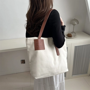 Minimalist off-white canvas tote bag with brown leather straps shown in a home setting