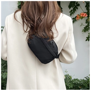 Detail of minimalist black nylon crossbody bag worn by a model in a beige blazer