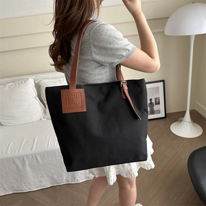 Minimalist black canvas tote bag with brown leather handles in a cozy home setting