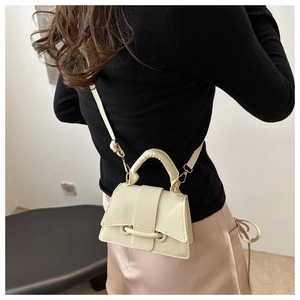 Detail showing the cream lychee-grain mini crossbody bag with gold hardware worn by model