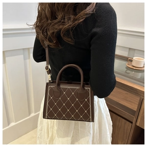 Dettaglio della mini borsa marrone scuro con cuciture a rombi e ricamo a cuore su modella