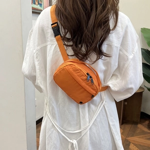 Orange nylon crossbody bag with adjustable strap shown on model in a casual setting