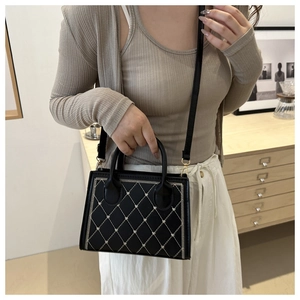Dettaglio di una borsa nera trapuntata con manico indossata da una modella in uno studio