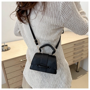 Detail of black lychee texture crossbody bag worn over a beige knit sweater on a model