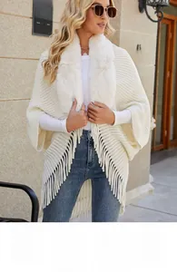 Close-up of white knit poncho featuring a fluffy faux fur collar and tassel hem detail