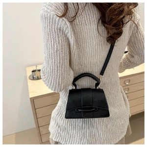 Detail of black lychee texture leather handbag on model in a minimalist indoor setting
