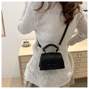 Detail of black litchi texture small square bag with leather buckle and fine strap