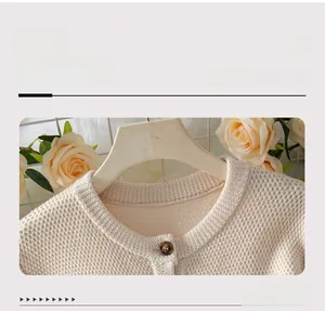 Detail of waffle knit crewneck on beige cardigan with amber buttons on wooden hanger