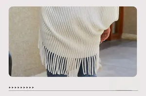 Close-up of white knitted poncho fabric with vertical stripes and long fringe tassels