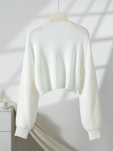 Detail of white chunky rib-knit cropped cardigan sweater on wooden hanger in soft lighting