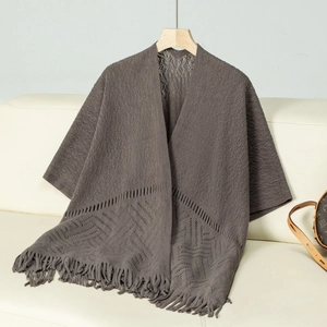Close-up of gray knit poncho featuring hollow weave texture and long fringe tassels