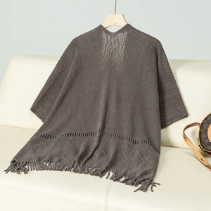 Detail of dark grey knit shawl with fine tassels and hollow texture on a leather sofa