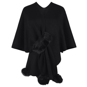 Women's black knitted poncho featuring plush fur trim and decorative pom-pom detailing