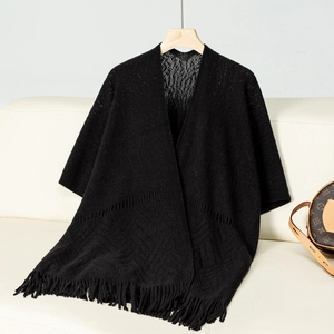 Detailed view of black knitted poncho featuring intricate hollow patterns and fringe tassels