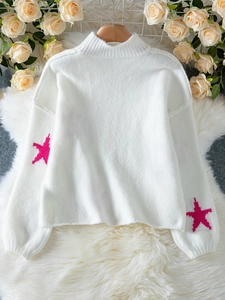 Detail of white turtleneck sweater featuring pink star motifs and soft knit texture