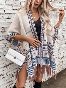Detail der geometrischen Jacquard-Strickerei und bunten Quasten am beigen Poncho