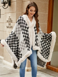 Detail of knit poncho featuring black and white plaid pattern and beige faux fur collar