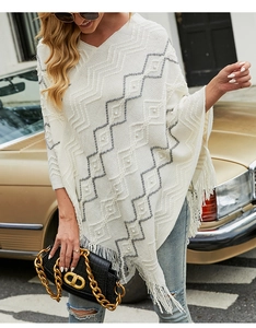 Detail of cream knit poncho with wave patterns, fringe hem, and pearl embellishments