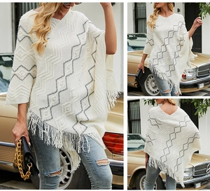 Detail of knitted white poncho featuring grey wave patterns, pearls, and tassel hemline