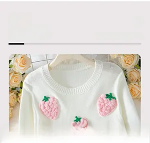 Detail of white knit sweater featuring 3D handmade crochet strawberry patches on the neckline