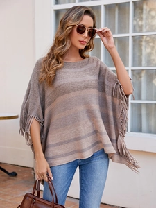 Close-up of knit striped poncho featuring long fringe details and earthy color tones