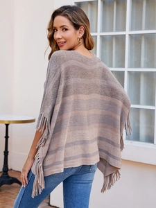 Detail of knitted striped poncho featuring long fringe hem and earth-tone patterns