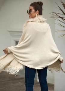 Detailed view of beige knitted poncho featuring a plush faux fur collar and fringe hem
