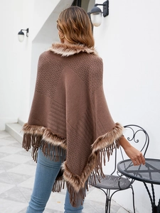 Outdoor back view of brown knit poncho featuring faux fur collar and fringe details