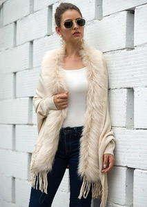 Close-up of elegant beige knit poncho with faux fur collar and decorative fringe trim