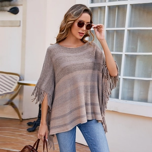 Women's knit poncho with horizontal brown stripes and fringe trim in outdoor setting