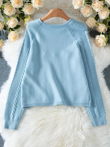 Detalle de jersey de punto azul claro con cuello redondo y textura trenzada en mangas