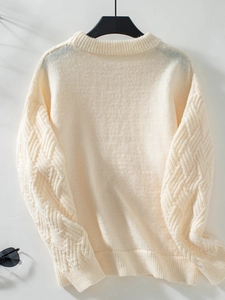 Detail of cream cable knit sweater showing geometric texture and soft shadow lighting