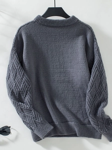 Macro detail of dark grey knit sweater showing 3D diamond cable stitch texture on sleeves