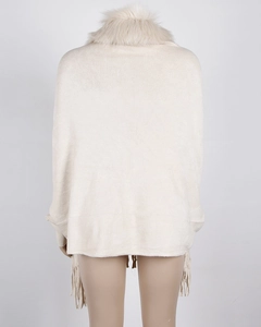 Detail of cream white knitted poncho featuring a faux fur collar and long tassel hemline