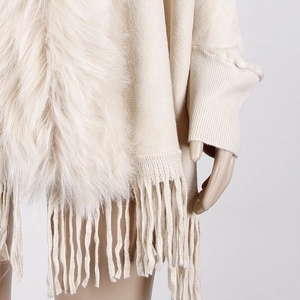 Close-up of beige knitted poncho featuring a plush faux fur collar and tassel fringe detail