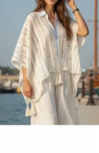 Close-up of white bohemian crochet knit shawl with tassel details against a harbor background