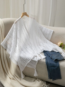 Detail of white crochet knit shawl featuring intricate geometric patterns and long tassels