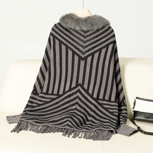 Detail of striped knitted poncho with faux fur collar and fringe tassels on a sofa