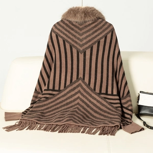 Detail of striped knit poncho with brown faux fur collar and fringed hem on a sofa