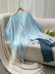 Detail of light blue knit shawl showing delicate hollow texture and fringe hem on a hanger