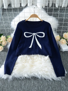 Detail of navy knit crop sweater with white bow pattern on a wooden hanger background
