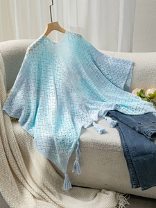 Detail of light blue hollow crochet lace shawl featuring elegant tassels on a sofa