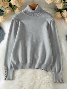 Detail of grey knit sweater cuff featuring four decorative gold buttons on a soft texture