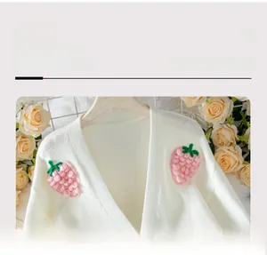 Détail de motifs fraises 3D tricotés sur un élégant cardigan blanc avec col en V