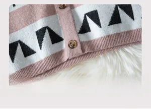 Detail of pink and white knit cardigan hem with geometric patterns and wood-textured buttons